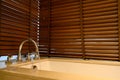 Close up ofÃÂ water flow from water tap into bathtub with wooden venetian blinds on background in bathroom